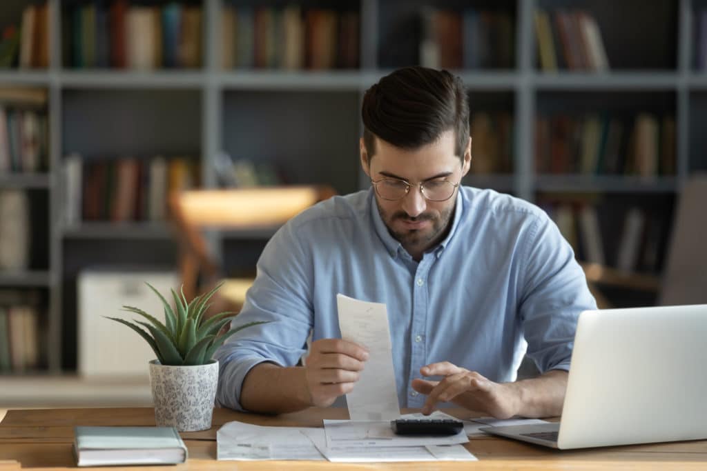 photo of man using a calculator and looking at a financial document