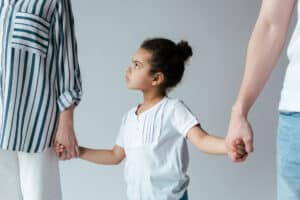 stock photo of sad child holding two parents hands