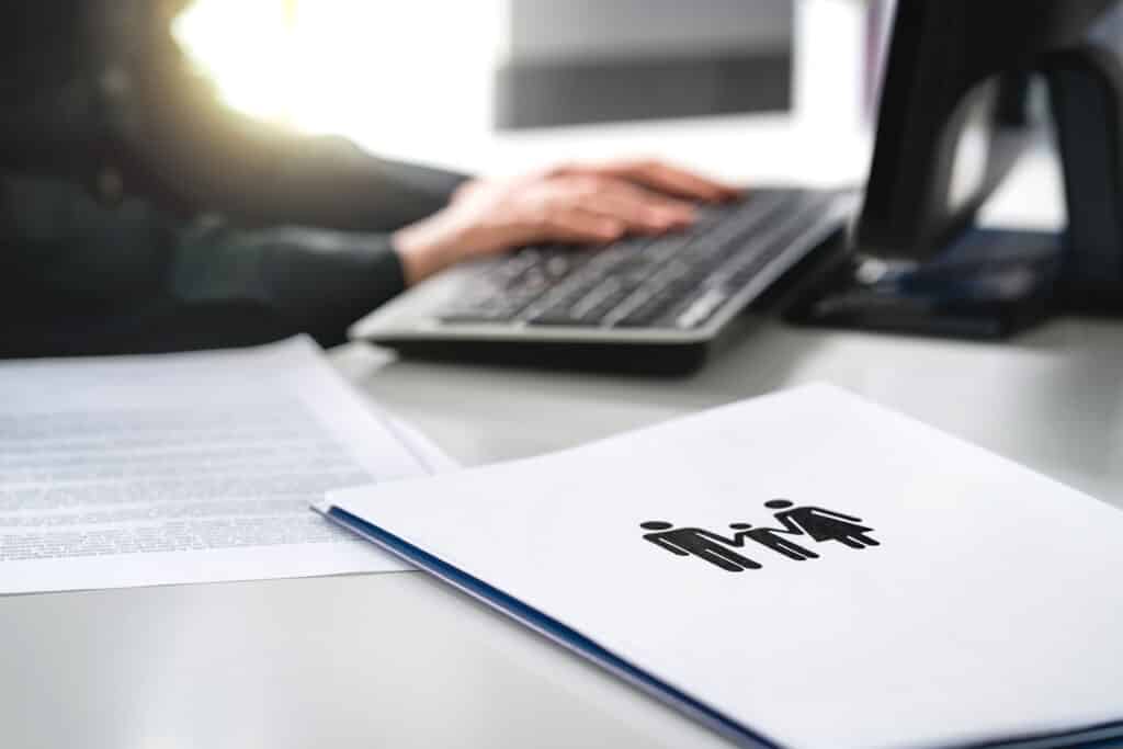 stock photo of a person at a computer with a family report in a folder sitting on desk next to keyboard